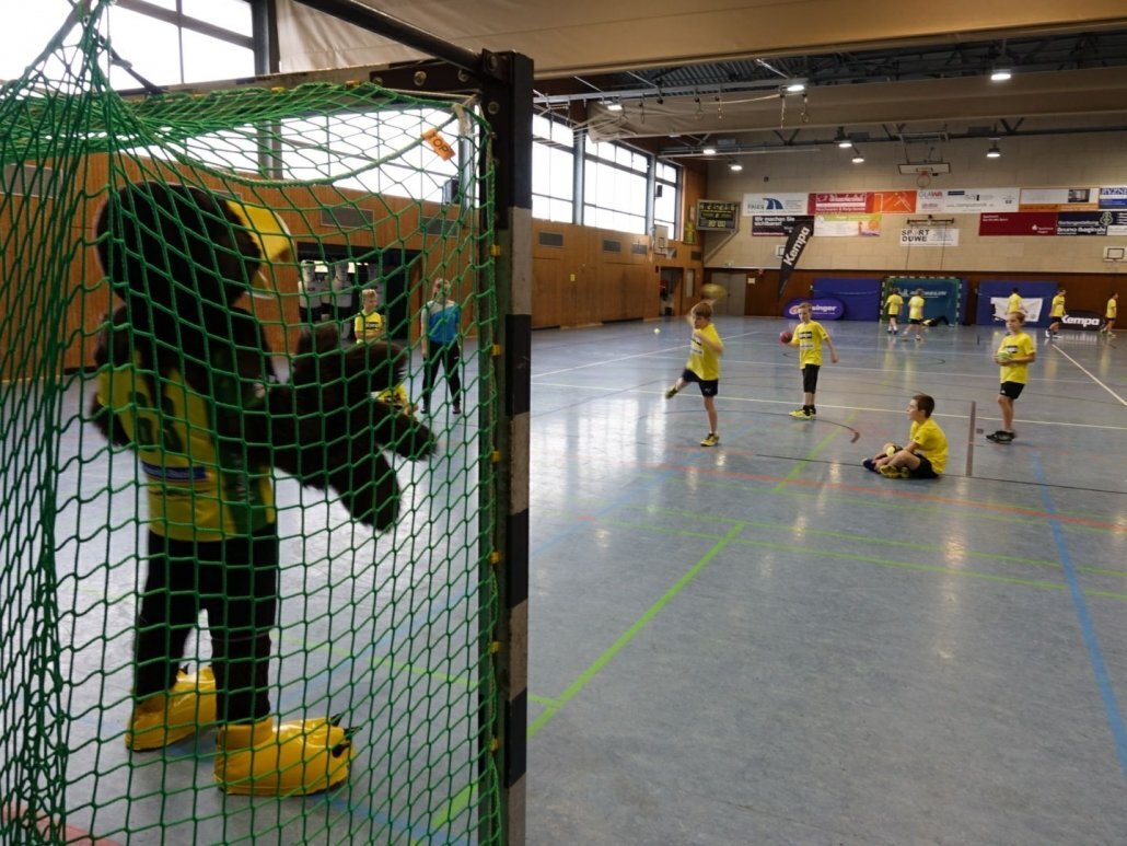 Maskottchen Hagen im Tor, junge im gelben Trikot wirft Handball